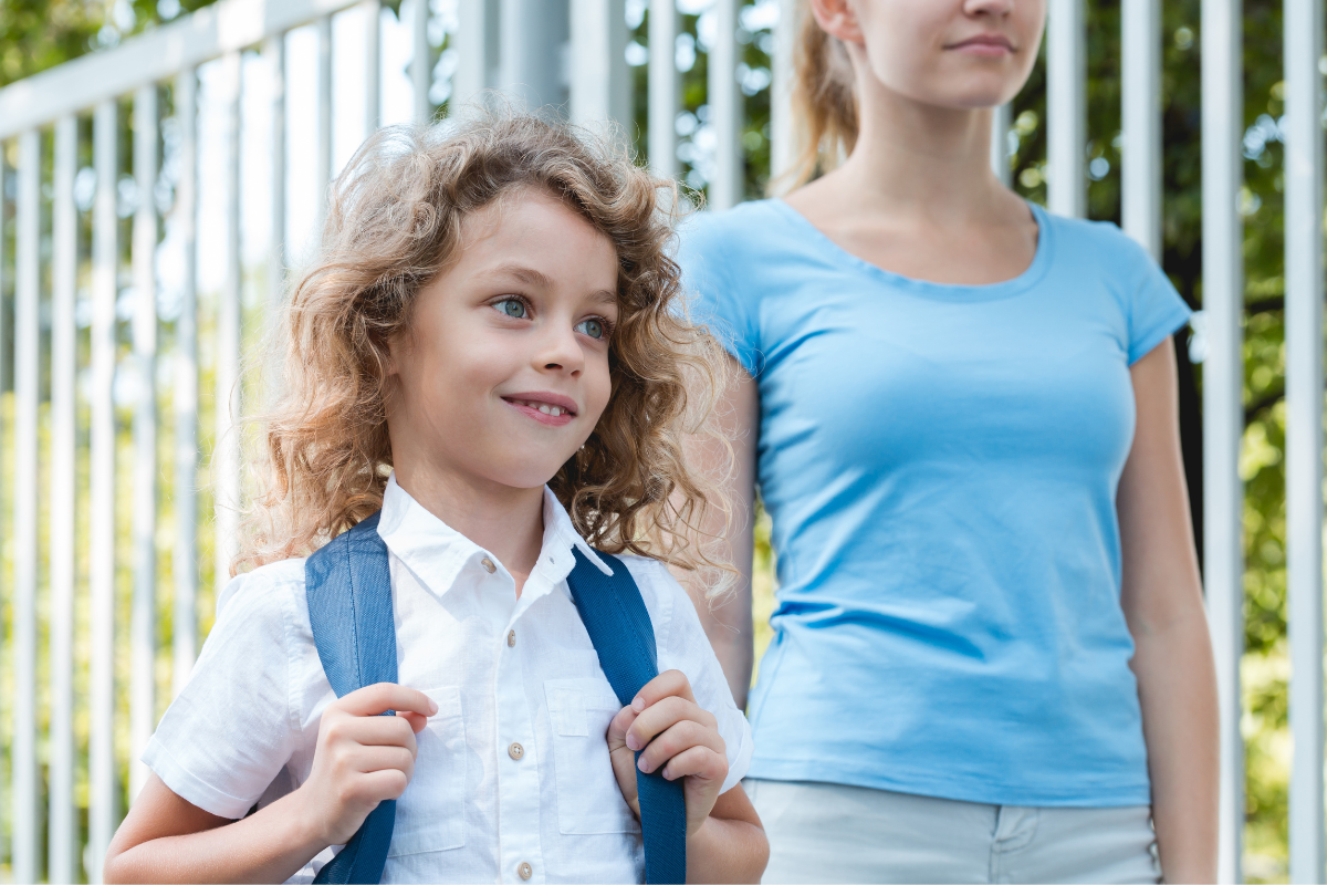 Boy smiling with backpack on walking to school with mother