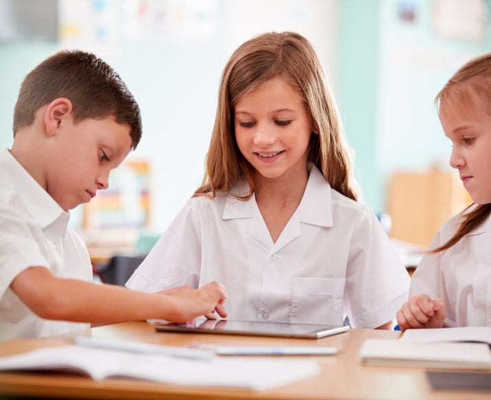 Three children sitting down at desk communicating with one another