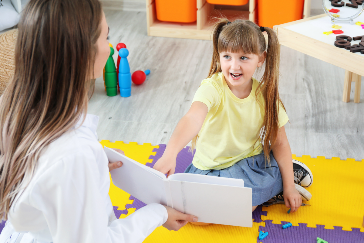 Young girl pointing to and reading from book held by speech therapist