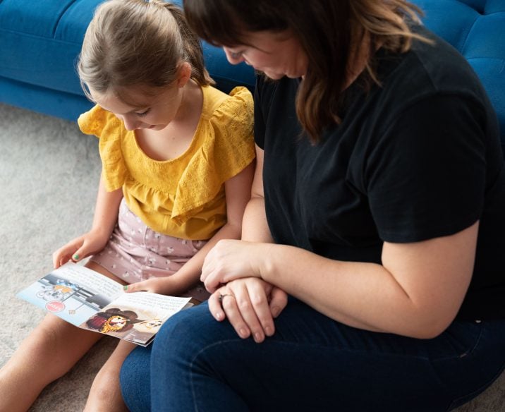 Child and adult sitting on floor reading book