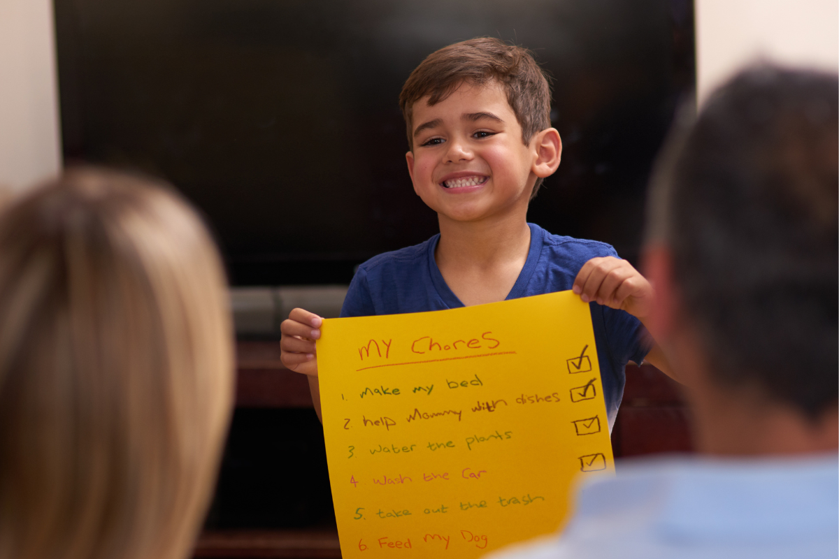 young boy holding up chore chart and smiling