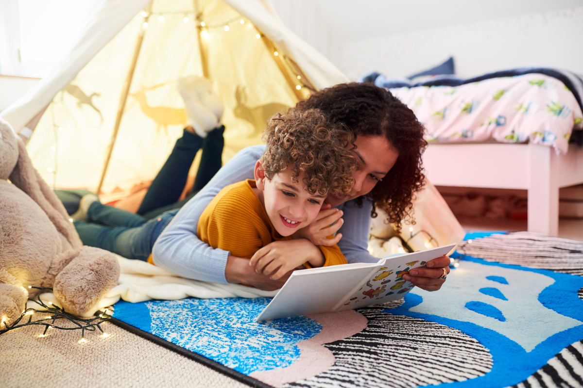 Mother cuddling son while laying on floor reading together