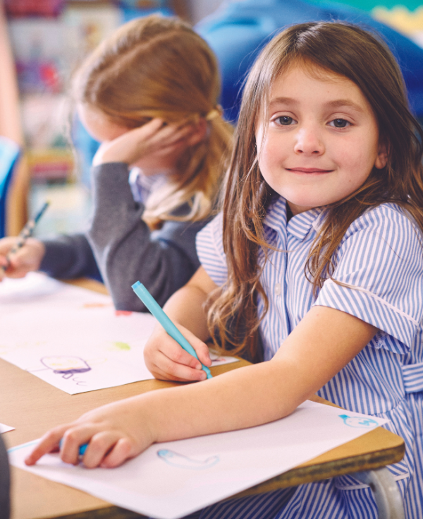 Young student wearing striped uniform seated at table doing a drawing activity