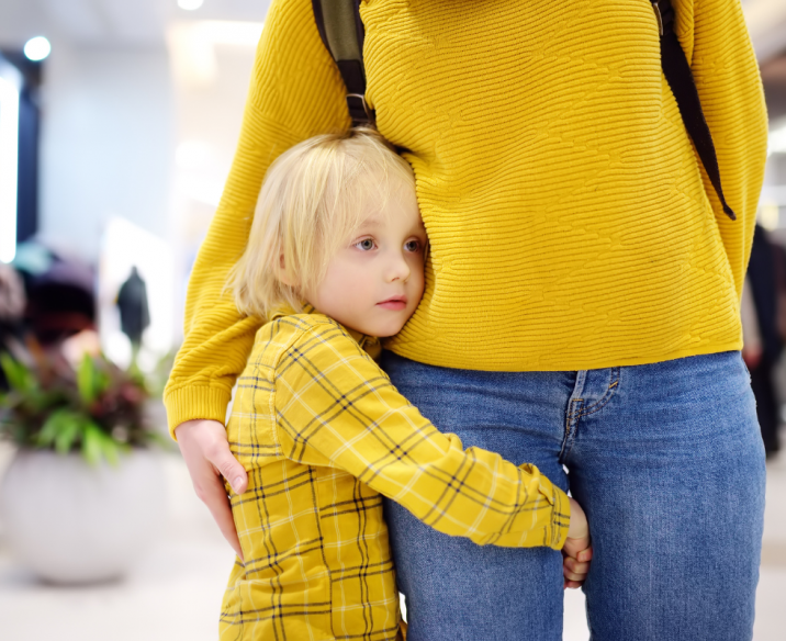 Young child looking sad and holding onto mother's leg