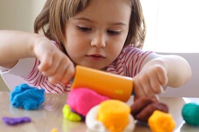 Child rolling play dough on table