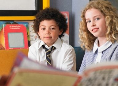 Boy and girl sitting in classroom having book read to them