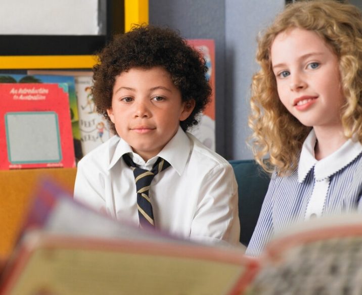 Boy and girl sitting in classroom having book read to them