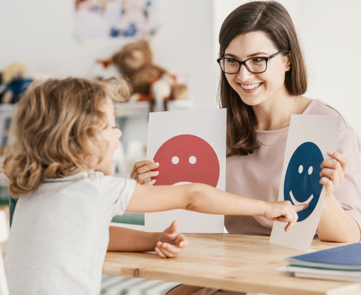 Psychologist holding up emotions images while child points at smiling face