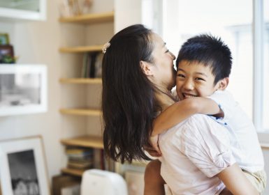 Mother holding son whole son wraps arms around neck and smiles