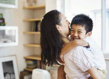 Mother holding son while son wraps arms around neck and smiles