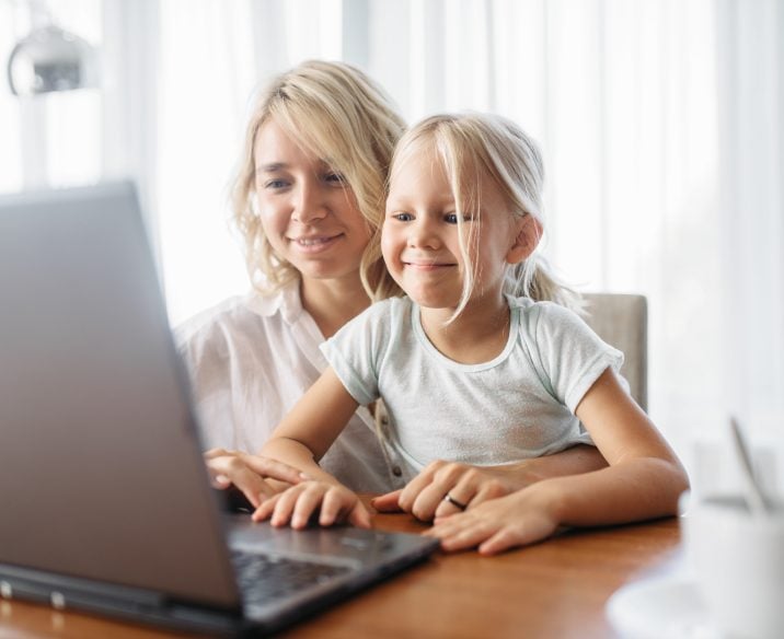 Smiling mother and child uses laptop at home