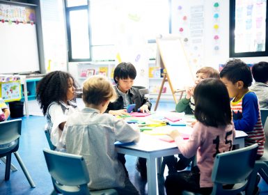 Group of children sit around table with coloured paper