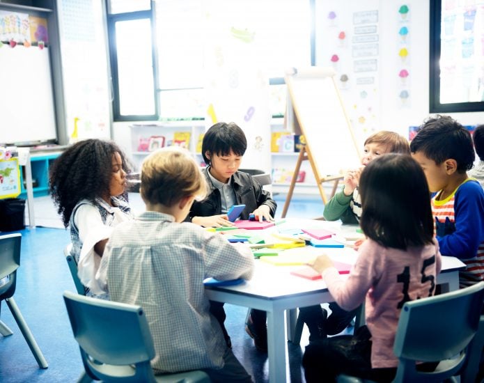 Group of children sit around table with coloured paper