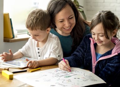 Mum sitting with son and daughter at table colouring in and playing on tablet