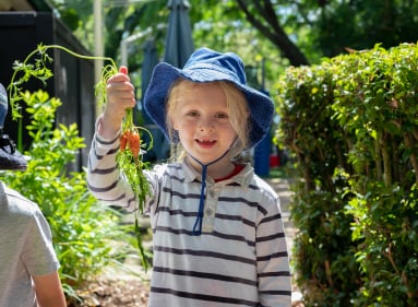 Girl near vegetable garden holding up carrot