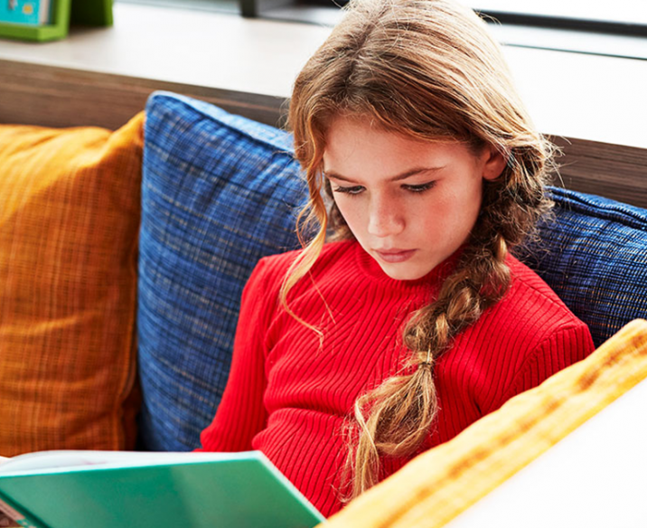 Young girl sitting on lounge reading a book