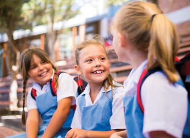 Girl in blue uniform sitting with friends in school playground