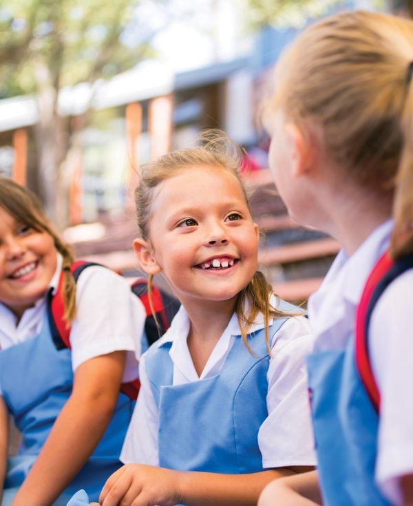 Girl in blue uniform sitting with friends in school playground