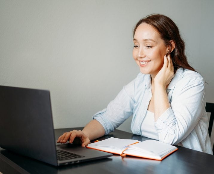 Smiling woman sitting at table look at laptop