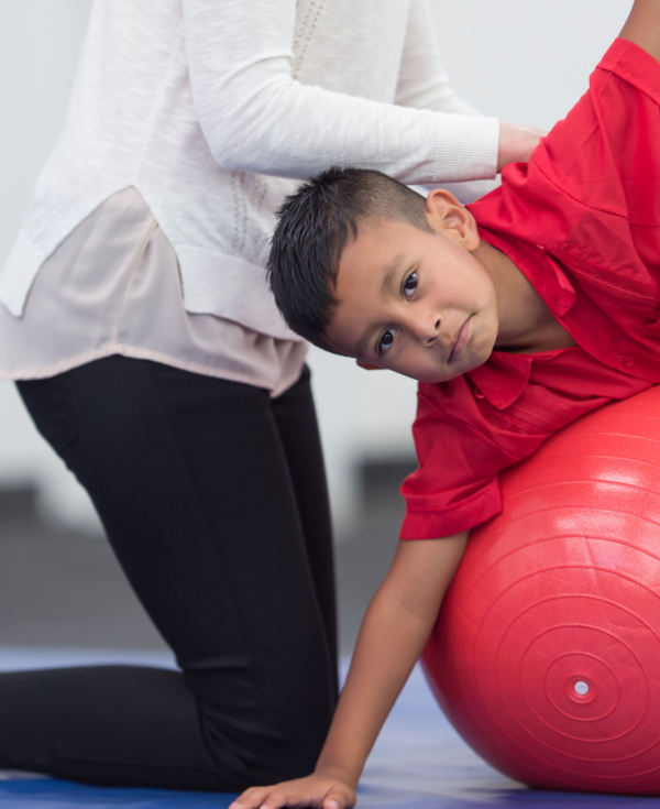 Therapist helping schoolboy balance on stomach on top of exercise ball