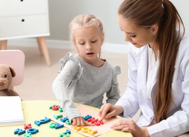 Young girls looking at letters of alphabet on table with speech pathologist