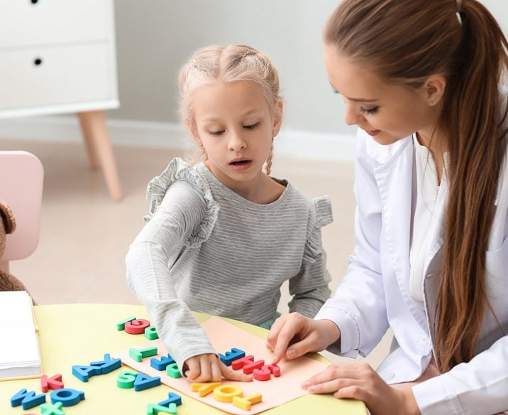 Young girls looking at letters of alphabet on table with speech pathologist