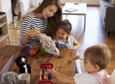 Mother participating in HIPPY family program playing with children on table at home