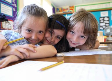 Three young school children smiling together in classroom