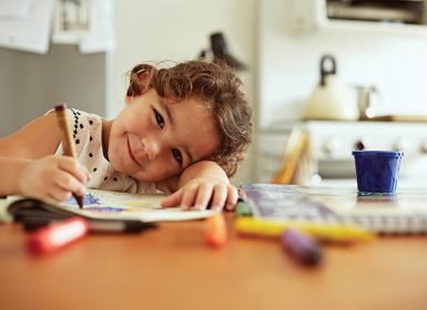 Young girl sitting down drawing at table and smiling