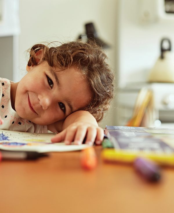 Young girl sitting down drawing at table and smiling