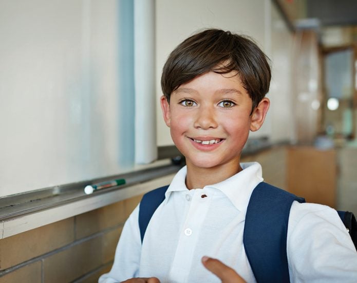 Young boy with brown eyes smiling next to whiteboard at school