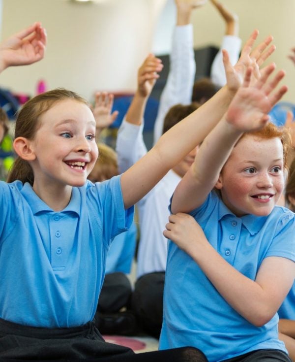 Group of school students in blue school uniform smiling with hands up in classroom