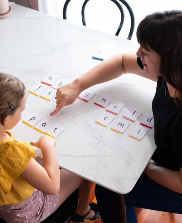 Phoneme flash cards laid out on table. Learning Links teacher points at the phoneme /a/ in pat while student sounds out word.