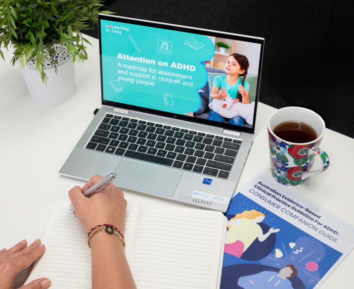 Laptop with course cover slide displayed while person's hand prepares to write notes in a book