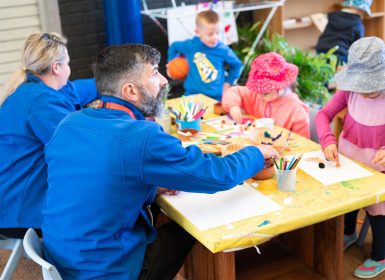 Officeworks staff sitting at table doing craft with Learning Links Preschool children