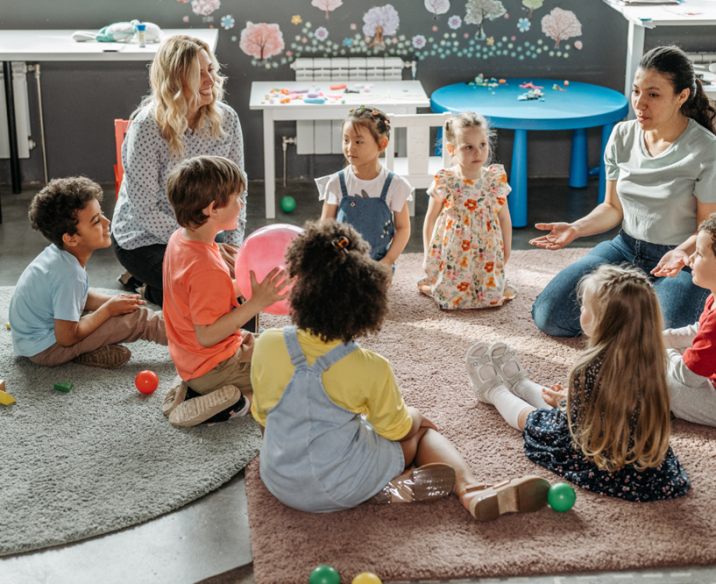 Two professionals sitting with group of preschool children
